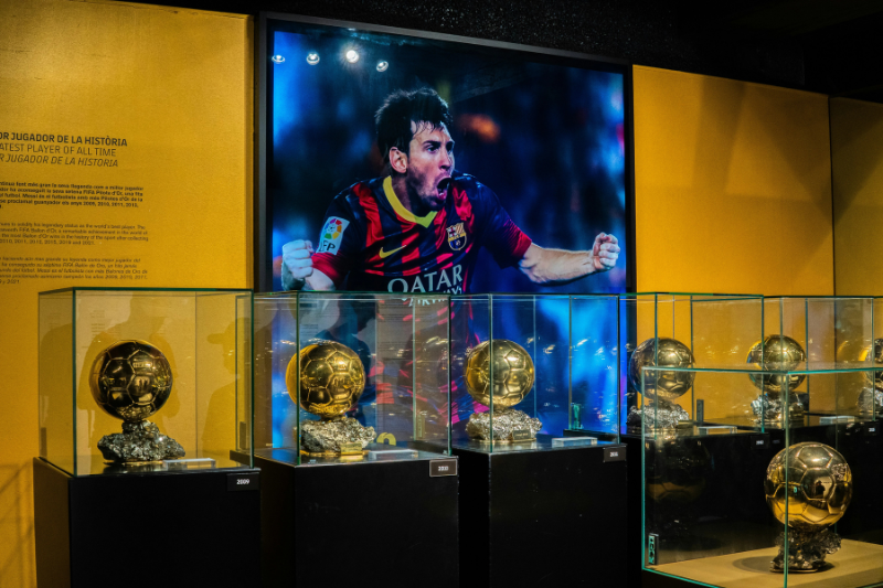 Lionel Messi stand with his ballon d'or trophies in front.