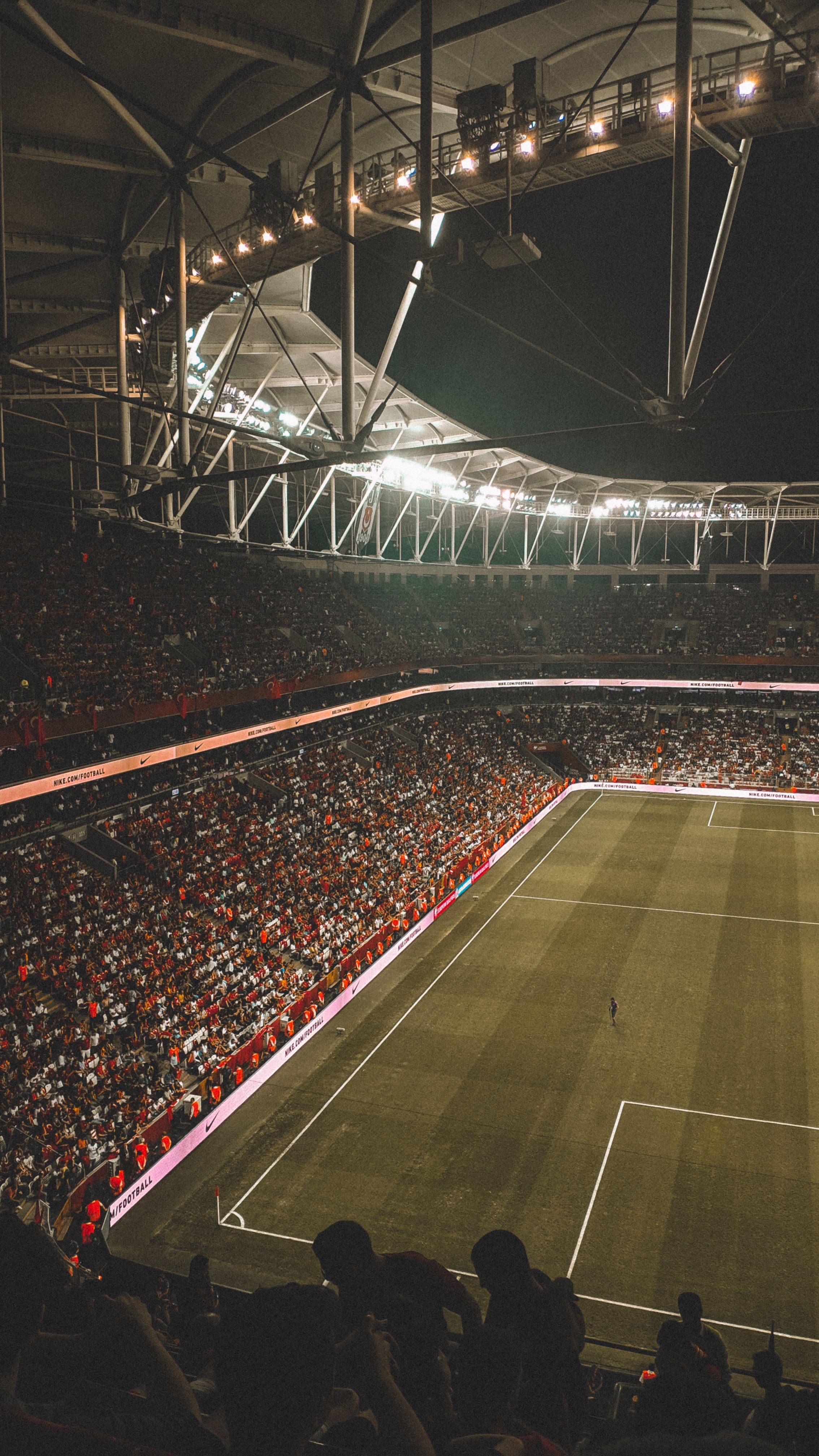 A football stadium at night, full of supporters, lit by floodlights during a match