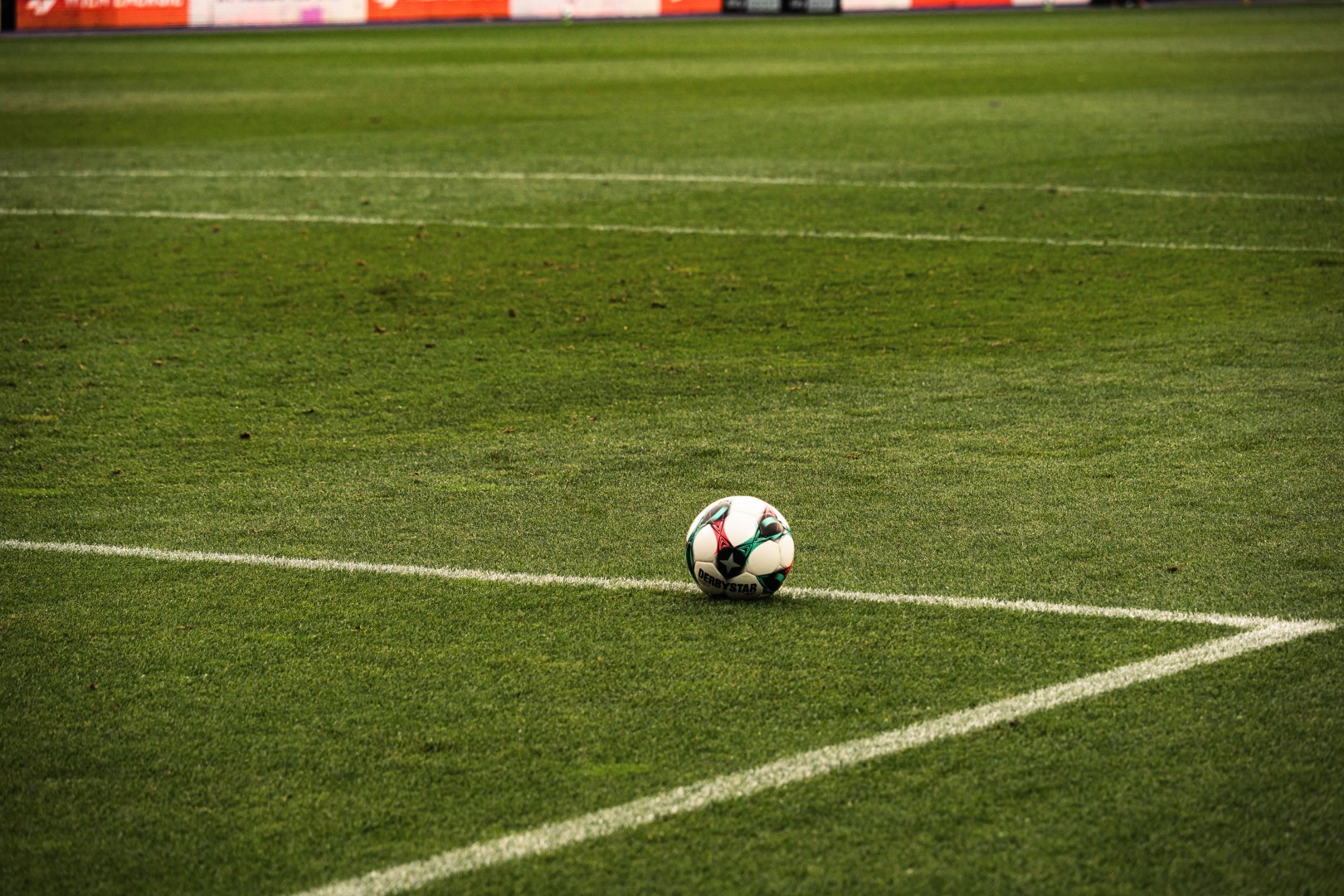 A football resting on the corner of an empty green pitch