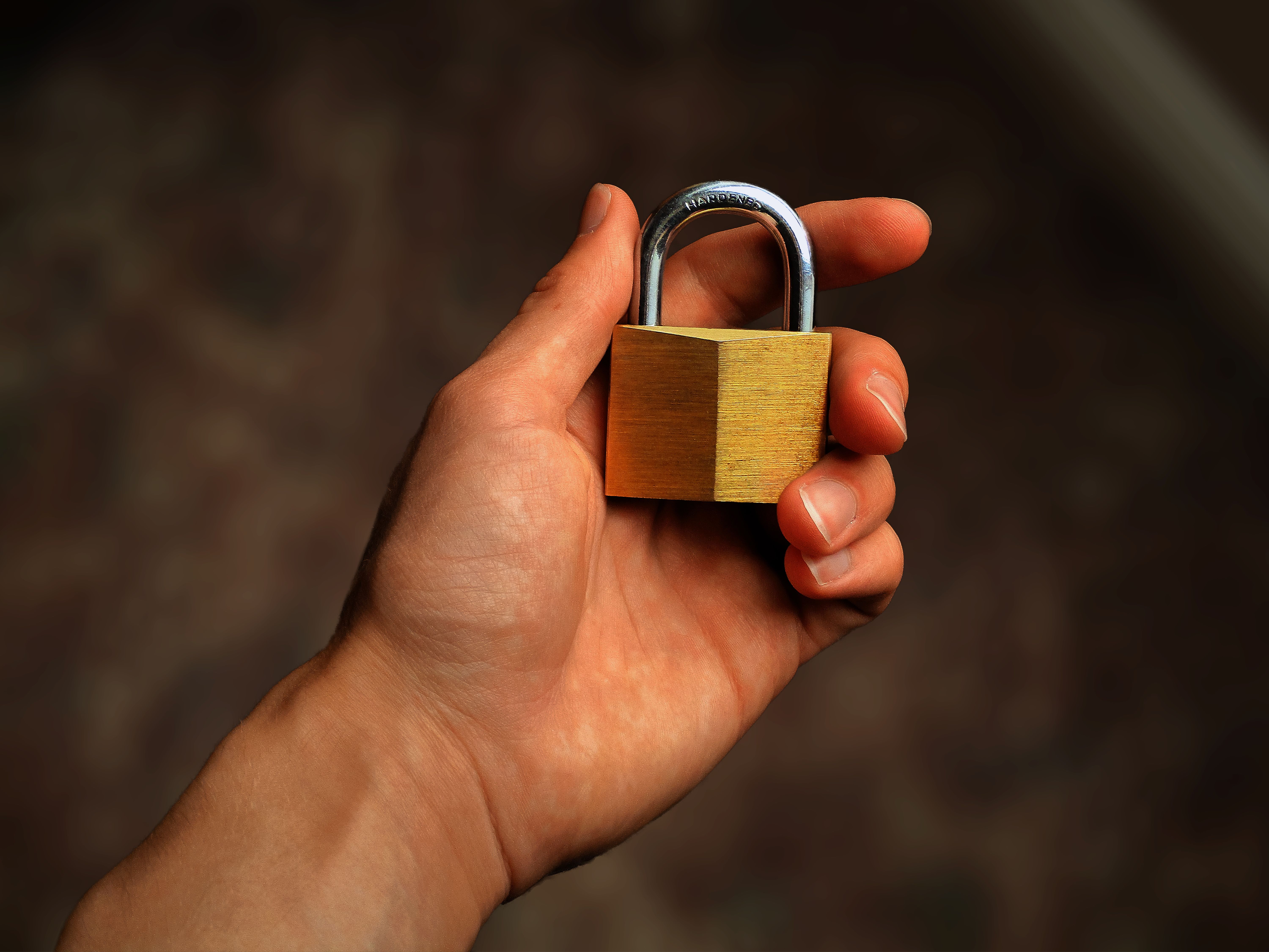 A hand holding a closed brass padlock
